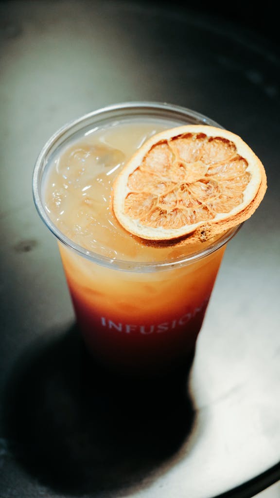 Cool citrus iced tea with a dried orange slice garnish in a plastic cup.