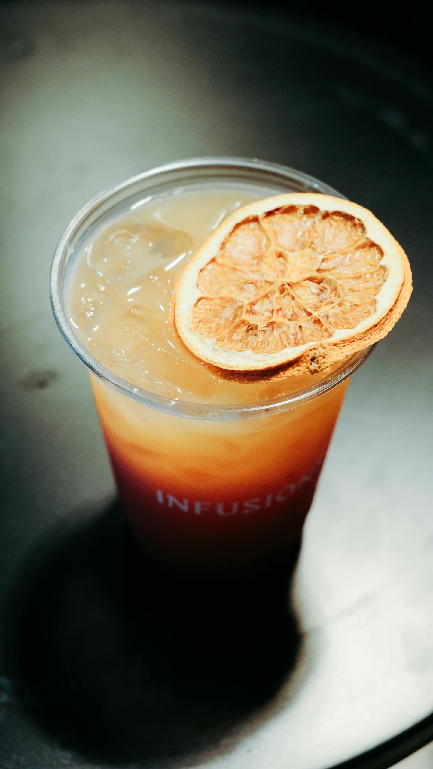 Cool citrus iced tea with a dried orange slice garnish in a plastic cup.