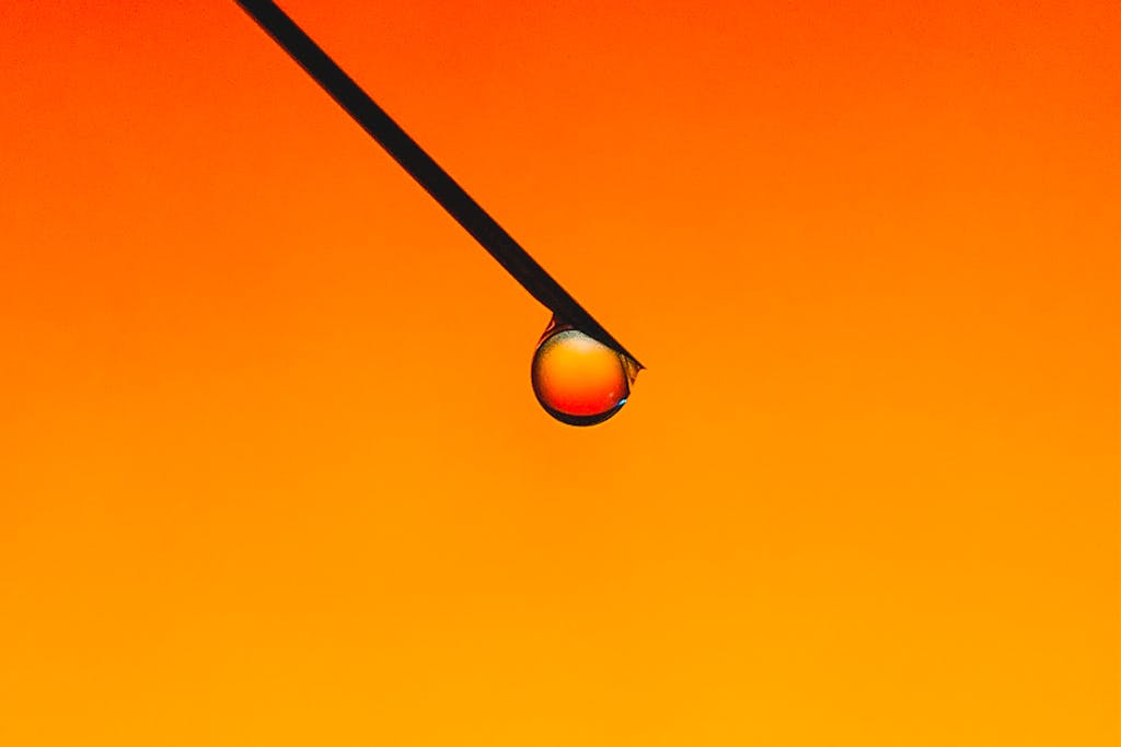 Extreme close-up of a water droplet on a needle with a vivid orange background.