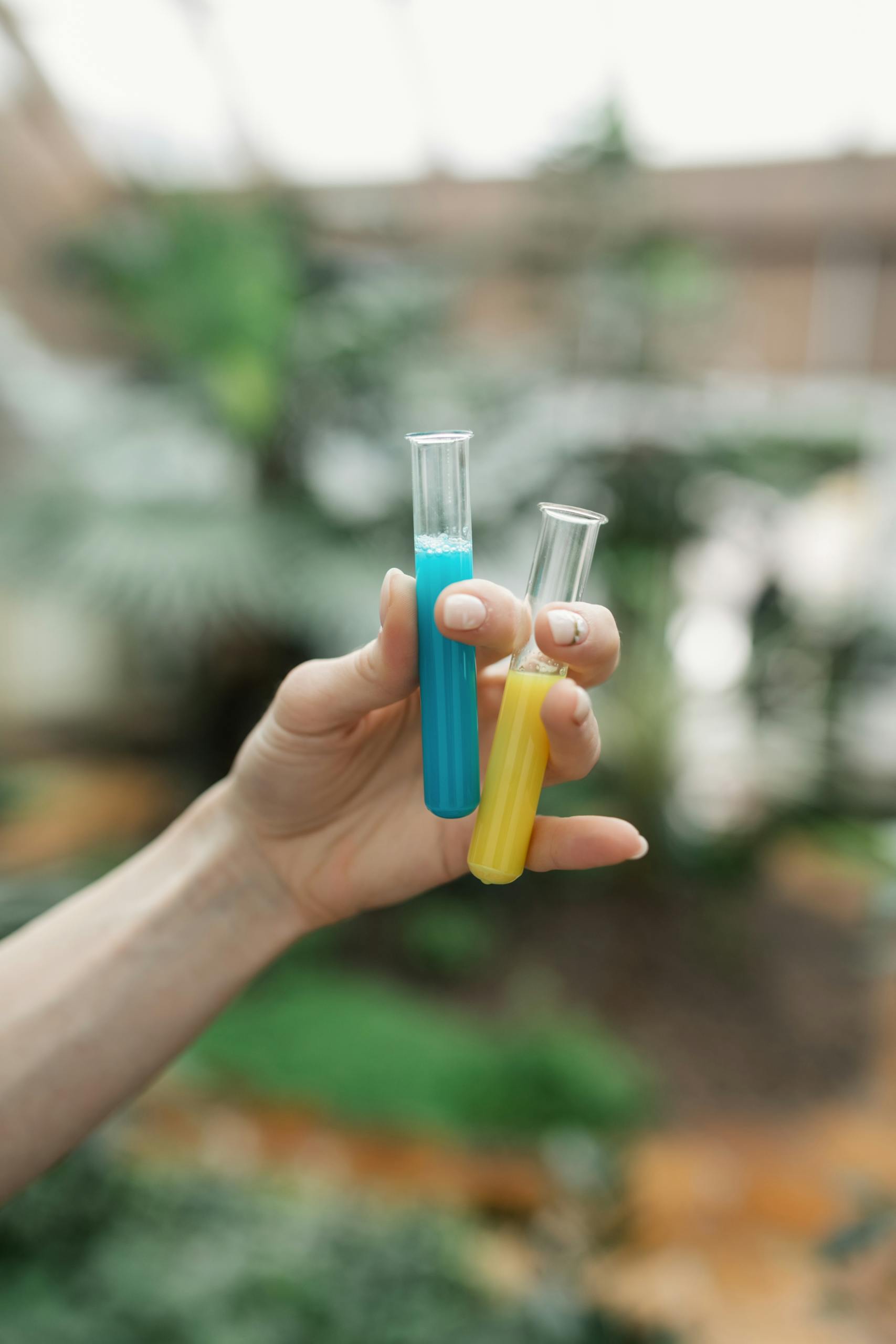 Vibrant close-up of hands holding blue and yellow test tubes in an outdoor setting.